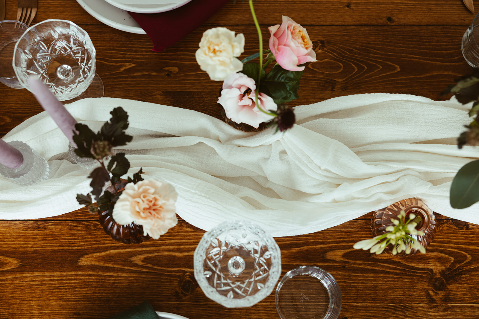 Een stijlvol ingedekte tafel houten met bloemen, glazen en kaarsen met de kleurtint paars en roze.