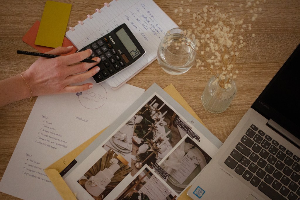 Bureau met laptop, documenten, checklist en rekenmachine tijdens de voorbereiding van een feest.